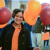 一位身穿橙色衬衫的年轻女子站在橙色和栗色气球旁边